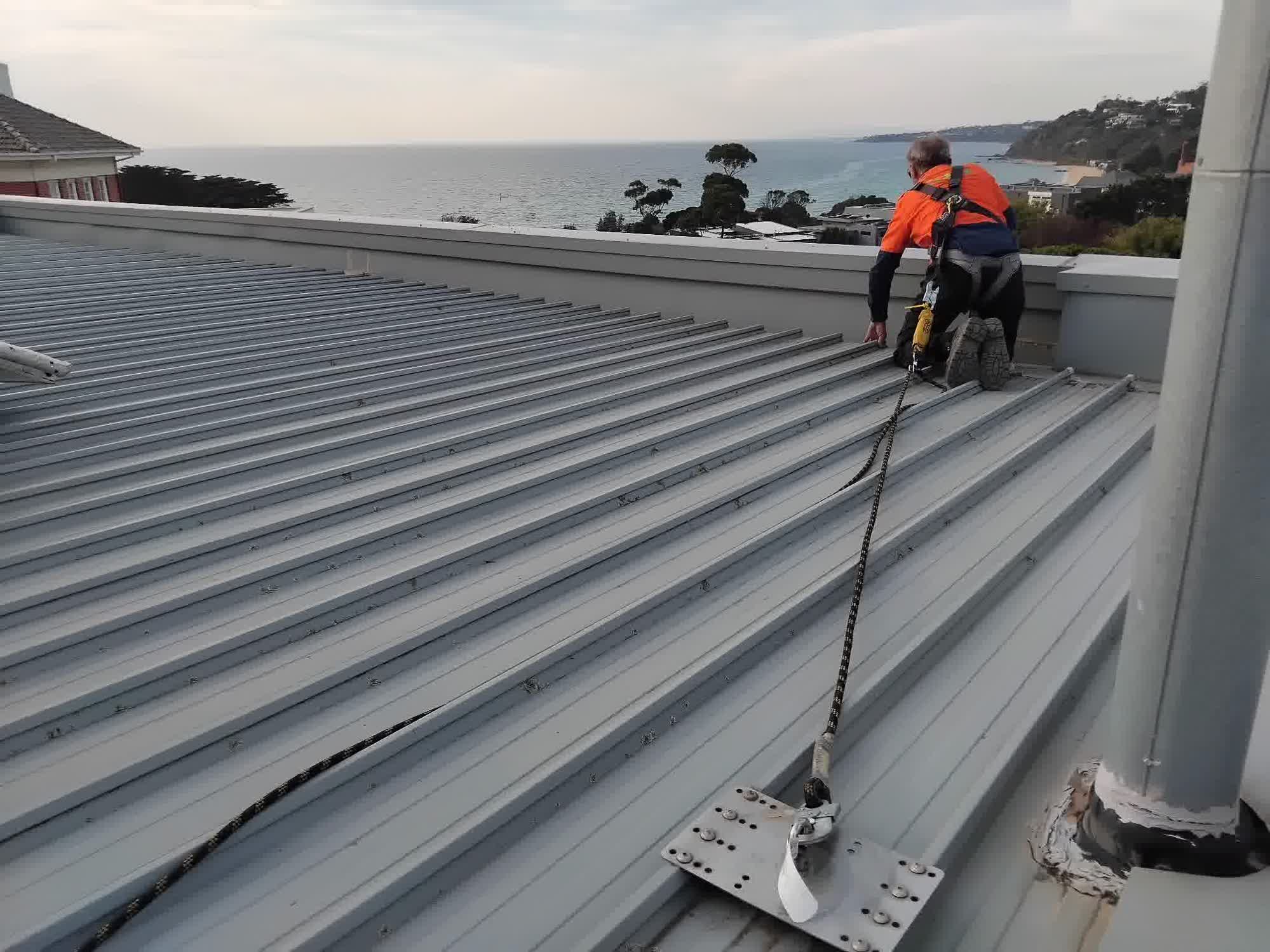 Technician inspecting a roof anchor point during a roof condition report on a coastal rooftop