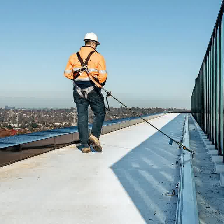Technician walking a commercial roof clipped into a rigid rail fall protection system